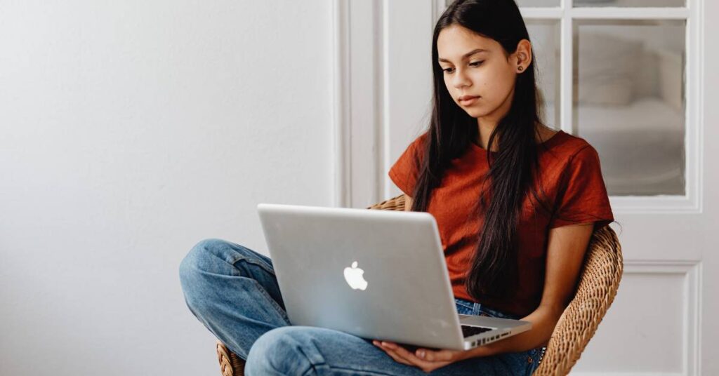 A teen sitting down with an Apple laptop 