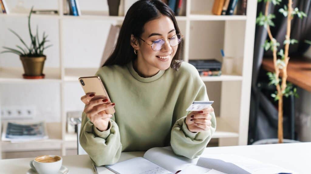 teen girl looking at her credit card, possibly buying something on her phone