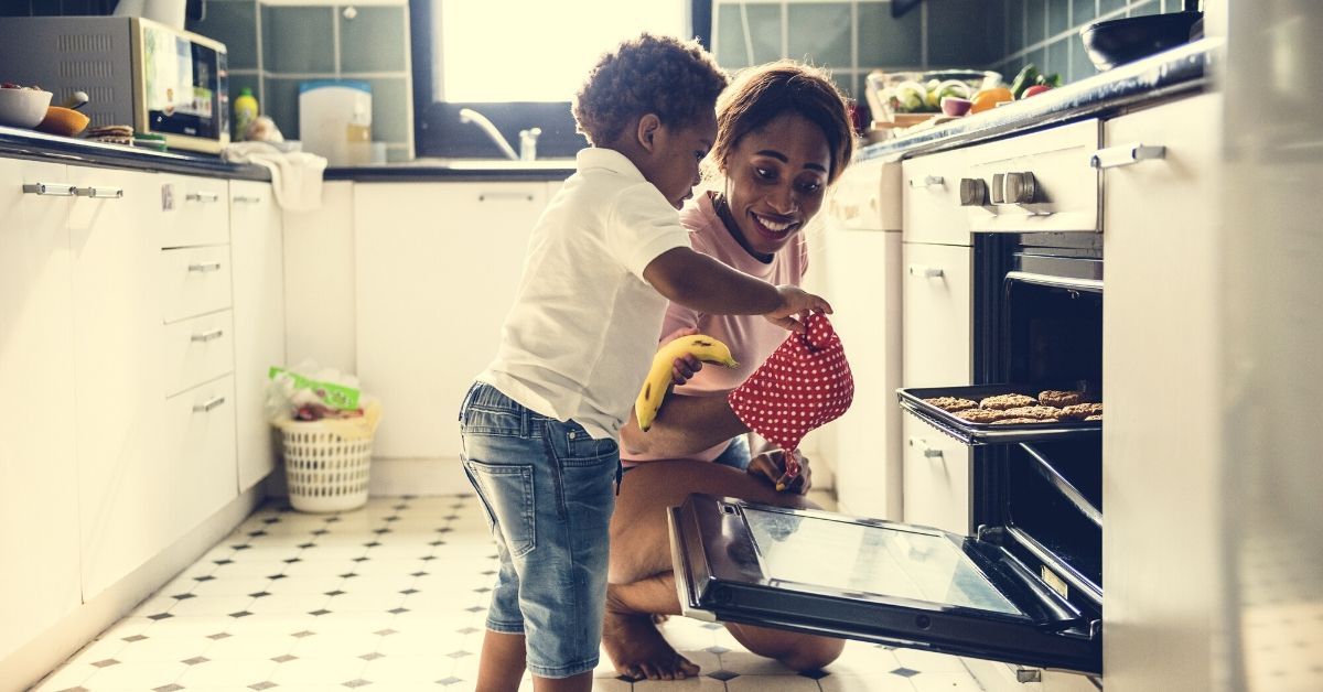 son attempting to take cookies out of oven as mother looks on