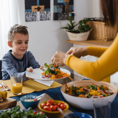 boy accepting salad from mother while learning table manners