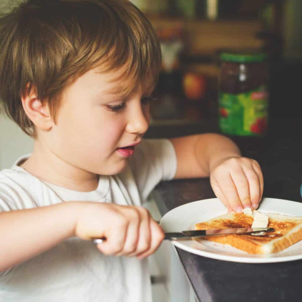 young boy spreading butter on toast independently