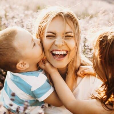 mother and kids laughing as infant son kisses mother on cheek