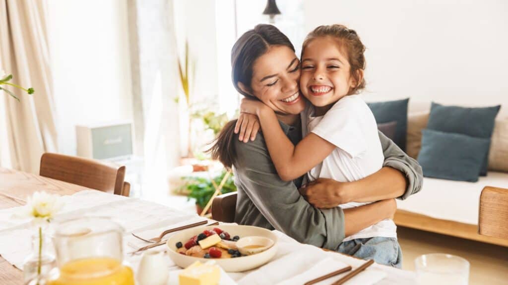 mother showing daughter affection during breakfast by hugging her