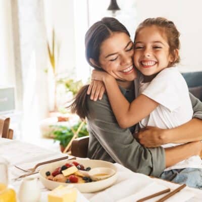mother showing daughter affection during breakfast by hugging her