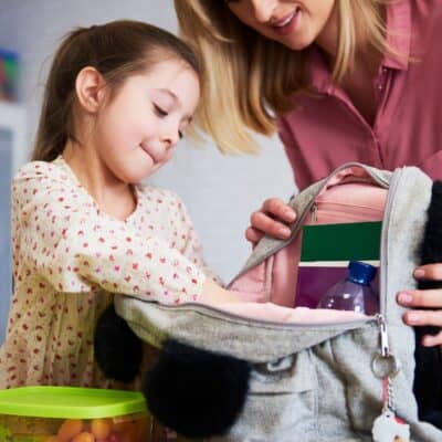 mother helping her daughter pack her backpack, teaching responsibility