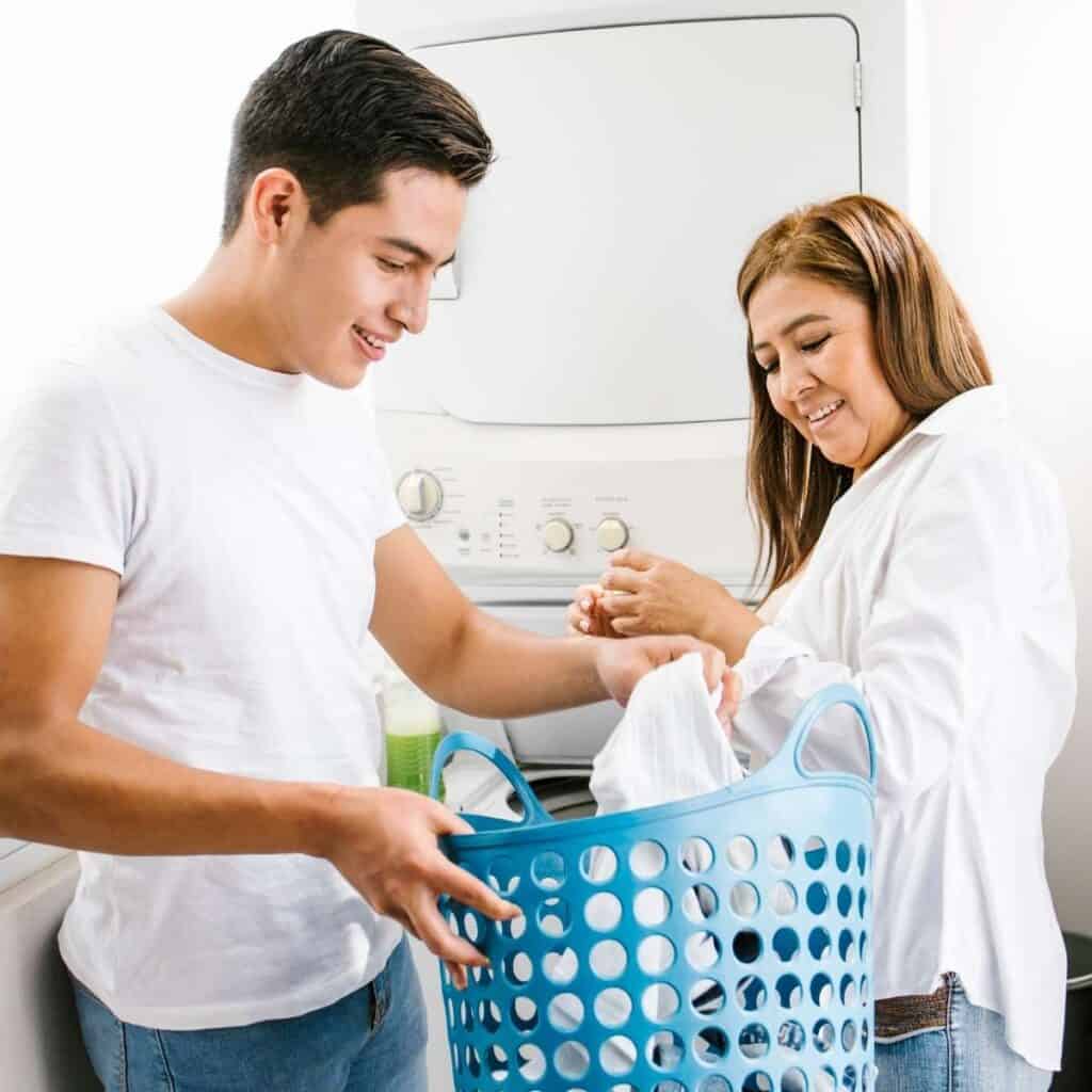 teen boy holding laundry basket while his mom looks on teaching him life skills