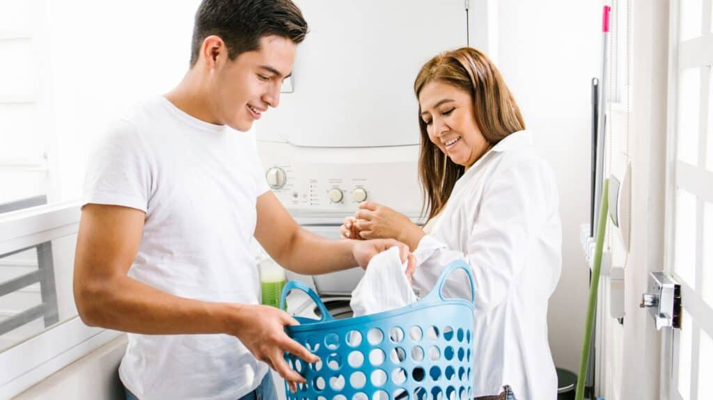 teen boy holding laundry with his mother looking on