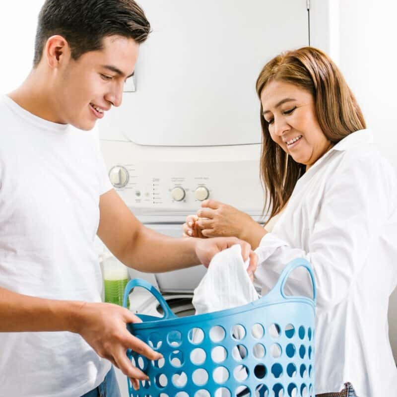 teen boy holding laundry with his mother looking on