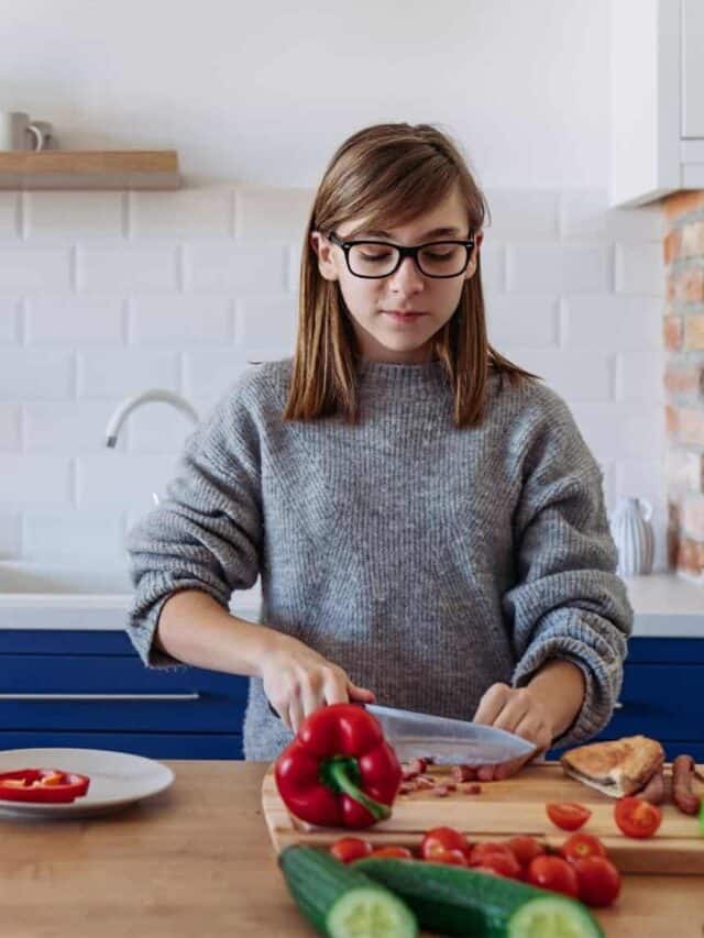 teen girl making dinner by slicing red peppers in a kitchen