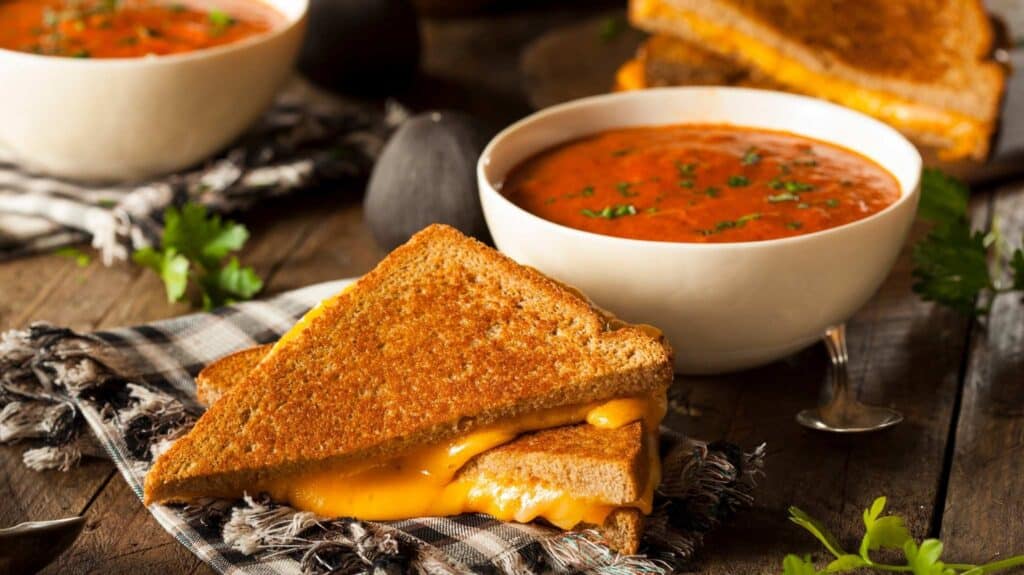 grilled cheese on a napkin next to a bowl of tomato soup