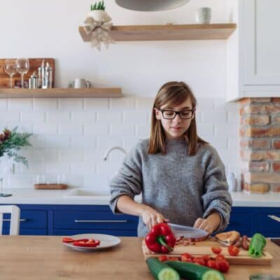 teen cutting peppers in a white kitchen