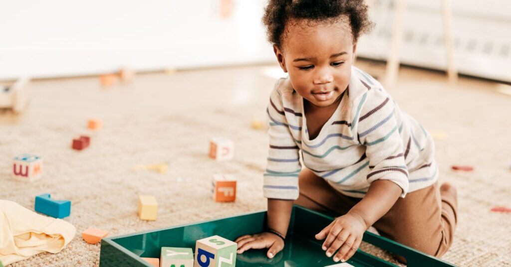 A toddler on a carpet putting blocks onto a tray