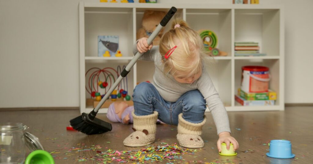 A little girl sweeping up glitter on the floor while also cleaning up other toys - practicing a number of executive functioning skills