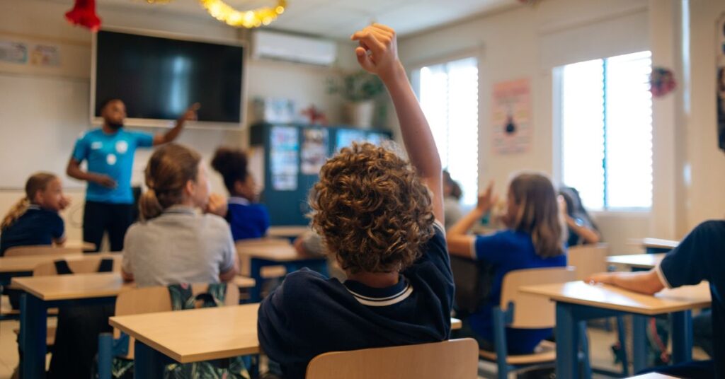 Children raising their hands in a school classroom showing their average attention span by age.