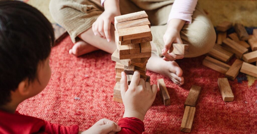 Two kids playing Jenga on the floor - one of the games that teach self control